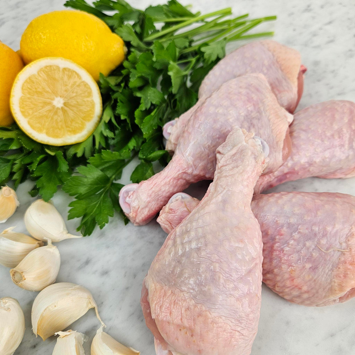 Raw pasture-raised chicken drumsticks on white marble with lemon, garlic, and fresh parsley — Wishbone Heritage Farms, South Carolina