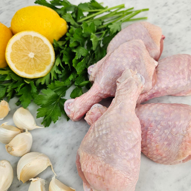 Raw pasture-raised chicken drumsticks on white marble with lemon, garlic, and fresh parsley — Wishbone Heritage Farms, South Carolina