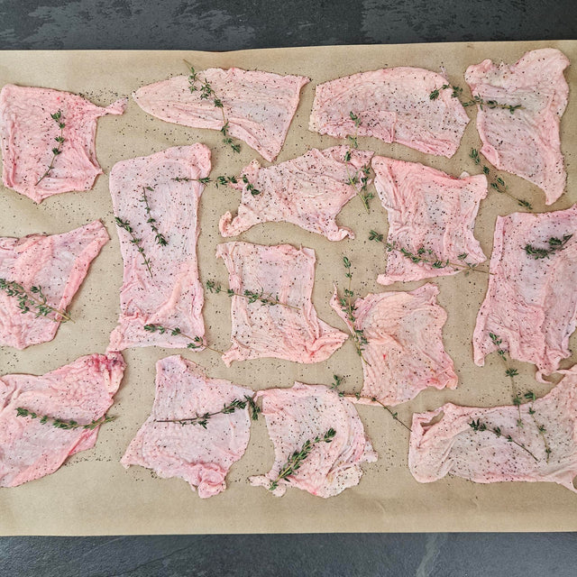Pasture-raised chicken skins seasoned with black pepper and fresh thyme on a parchment-lined baking sheet — Wishbone Heritage Farms, Saint George, SC