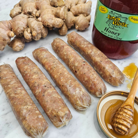 Raw pasture-raised honey ginger chicken sausage links on white marble with fresh ginger root and wildflower honey — Wishbone Heritage Farms, Saint George, SC