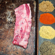 Pasture-raised heritage breed pork baby back ribs on a seasoned sheet pan with dry rub spices — brown sugar, paprika, mustard, and black pepper — Wishbone Heritage Farms, Saint George, SC