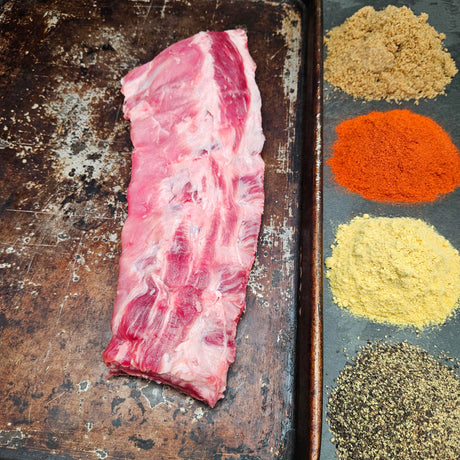 Pasture-raised heritage breed pork baby back ribs on a seasoned sheet pan with dry rub spices — brown sugar, paprika, mustard, and black pepper — Wishbone Heritage Farms, Saint George, SC