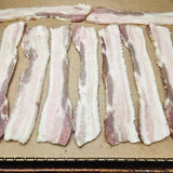 Raw pasture-raised heritage breed pork bacon strips laid out on a parchment-lined baking rack ready to cook — Wishbone Heritage Farms, Saint George, SC