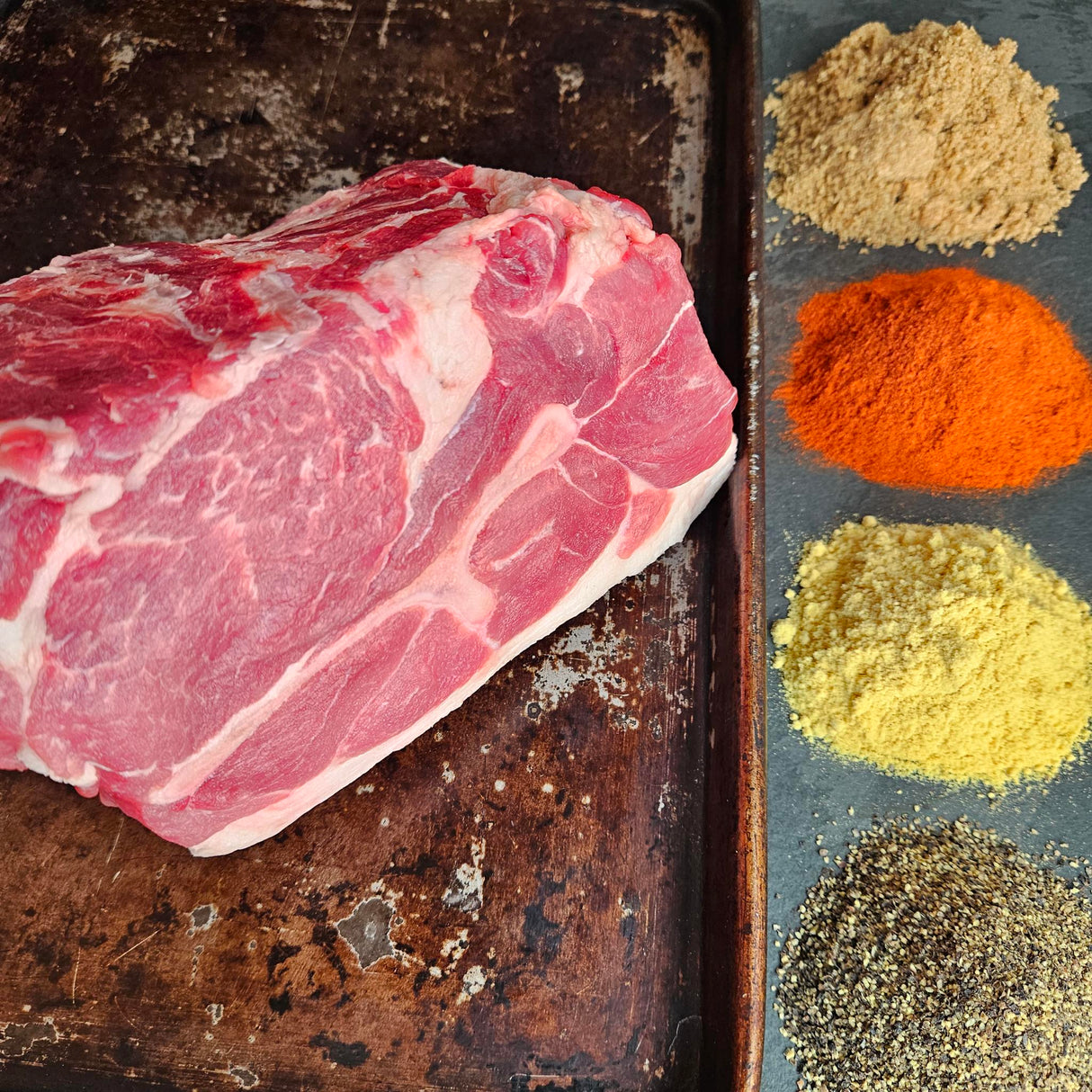 Pasture-raised heritage breed pork Boston butt on a seasoned sheet pan with dry rub spices — brown sugar, paprika, mustard, and black pepper — Wishbone Heritage Farms, Saint George, SC