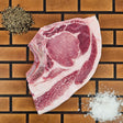 Pasture-raised heritage breed thick-cut blade pork chop on an end-grain butcher block with flake salt and cracked pepper — Wishbone Heritage Farms, Saint George, SC