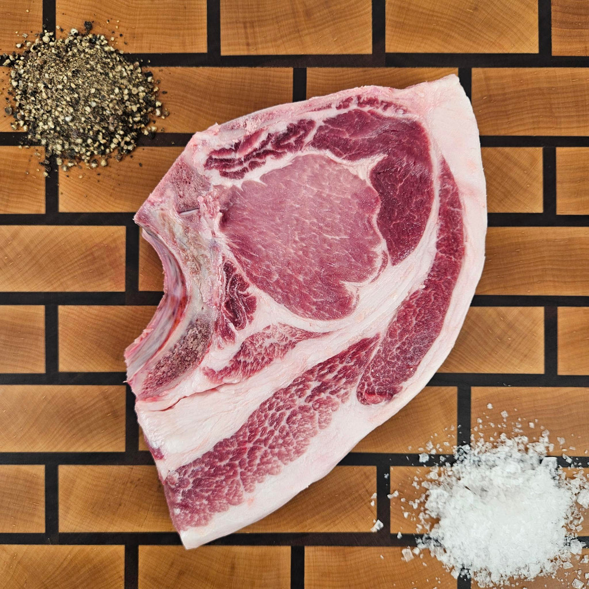 Pasture-raised heritage breed thick-cut blade pork chop on an end-grain butcher block with flake salt and cracked pepper — Wishbone Heritage Farms, Saint George, SC