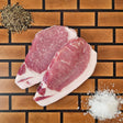 Pasture-raised heritage breed boneless center cut pork chops on an end-grain butcher block with flake salt and cracked pepper — Wishbone Heritage Farms, Saint George, SC