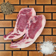 Pasture-raised heritage breed thin center cut bone-in pork chop on an end-grain butcher block with flake salt and cracked pepper — Wishbone Heritage Farms, Saint George, SC