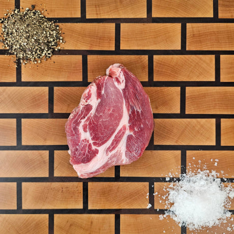 Pasture-raised heritage breed pork coppa steak on an end-grain butcher block with flake salt and cracked pepper — Wishbone Heritage Farms, Saint George, SC