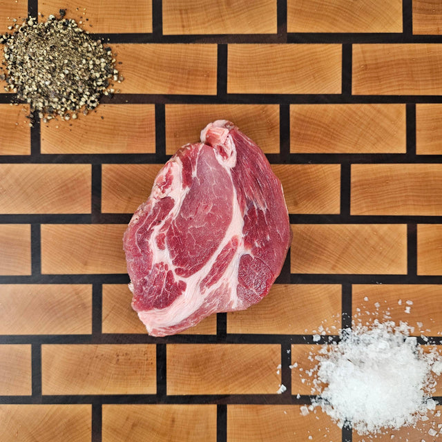 Pasture-raised heritage breed pork coppa steak on an end-grain butcher block with flake salt and cracked pepper — Wishbone Heritage Farms, Saint George, SC