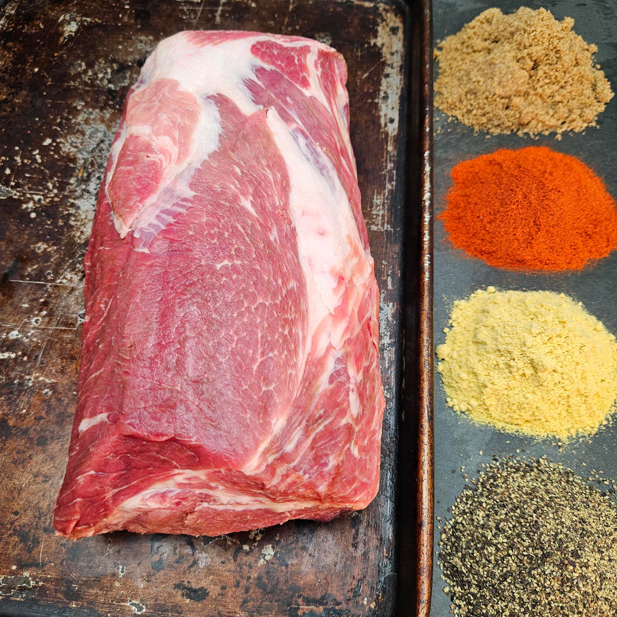 Pasture-raised heritage breed pork coppa on a seasoned sheet pan with dry rub spices — brown sugar, paprika, mustard, and black pepper — Wishbone Heritage Farms, Saint George, SC
