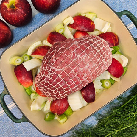 Raw pasture-raised heritage breed pork fresh inside ham, boneless and netted, on apples and fennel in a green roasting pan — Wishbone Heritage Farms, Saint George, SC