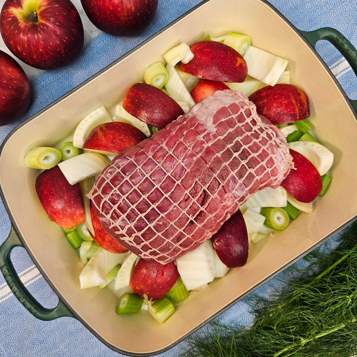 Raw pasture-raised heritage breed pork fresh leg tip, boneless and netted, on apples and fennel in a green roasting pan — Wishbone Heritage Farms, Saint George, SC
