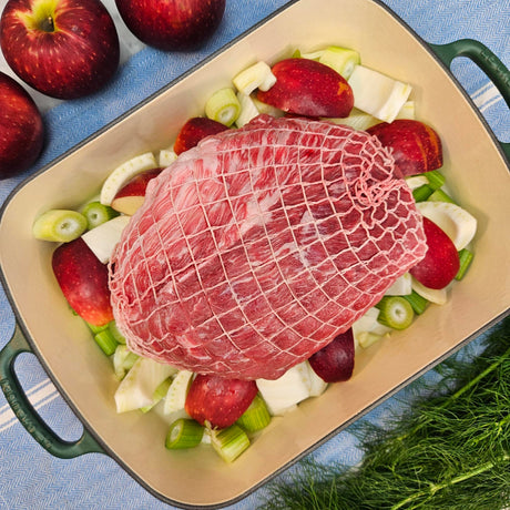 Raw pasture-raised heritage breed pork fresh outside ham, boneless and netted, on apples and fennel in a green roasting pan — Wishbone Heritage Farms, Saint George, SC