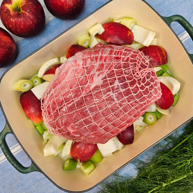 Raw pasture-raised heritage breed pork fresh outside ham, boneless and netted, on apples and fennel in a green roasting pan — Wishbone Heritage Farms, Saint George, SC