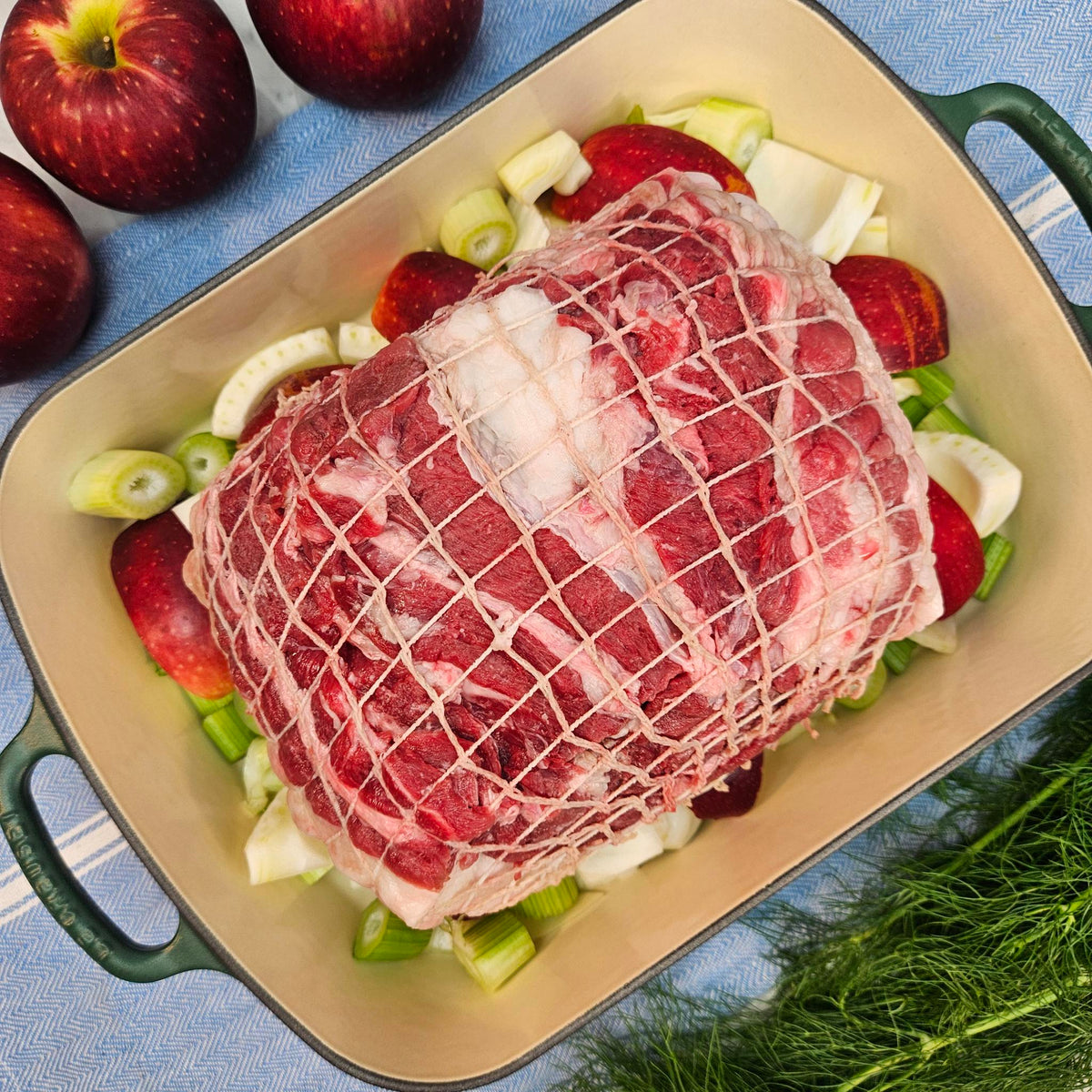 Raw pasture-raised heritage pork sirloin roast in netting on apples and fennel in a green roasting pan — Wishbone Heritage Farms, Saint George, SC