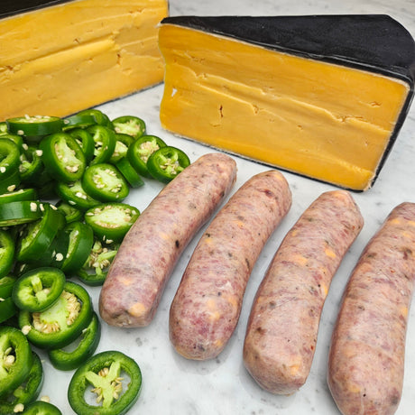 Raw pasture-raised heritage pork jalapeño cheddar sausage links on white marble with sliced fresh jalapeños and a wedge of aged cheddar — Wishbone Heritage Farms, Saint George, SC