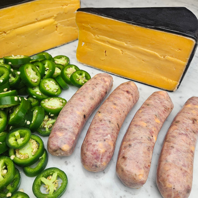 Raw pasture-raised heritage pork jalapeño cheddar sausage links on white marble with sliced fresh jalapeños and a wedge of aged cheddar — Wishbone Heritage Farms, Saint George, SC