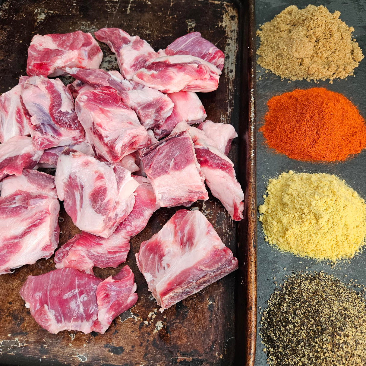Pasture-raised heritage breed pork riblets on a seasoned sheet pan with dry rub spices — brown sugar, paprika, mustard, and black pepper — Wishbone Heritage Farms, Saint George, SC