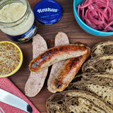 Pasture-raised heritage pork kielbasa pan-seared then sliced, on a wooden board with horseradish, whole grain mustard, pickled red onions, and dark rye bread — Wishbone Heritage Farms, Saint George, SC