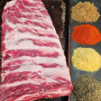 Pasture-raised heritage breed pork St Louis ribs on a seasoned sheet pan with dry rub spices — brown sugar, paprika, mustard, and black pepper — Wishbone Heritage Farms, Saint George, SC