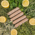 Raw pasture-raised lemon and herb chicken sausage links on a bed of fresh rosemary, thyme, sage, oregano, and parsley with sliced lemon — Wishbone Heritage Farms, Saint George, SC
