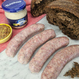 Raw pasture-raised heritage pork biala kielbasa on white marble with dark rye bread, horseradish, and whole grain mustard — Wishbone Heritage Farms, Saint George, SC