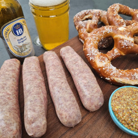 Raw pasture-raised pork garlic bratwurst on a wooden board with soft pretzels, whole grain mustard, and a poured beer — Wishbone Heritage Farms, South Carolina