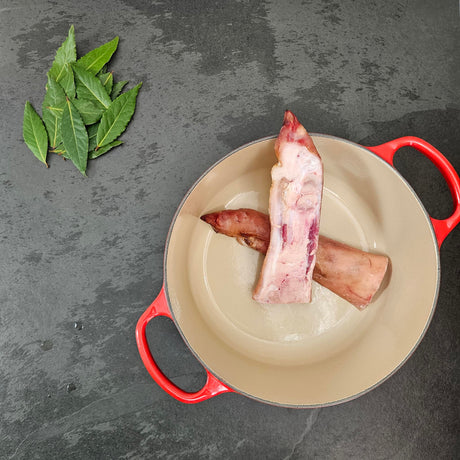 Pasture-raised split pig foot in a red Le Creuset Dutch oven with fresh bay leaves — Wishbone Heritage Farms, Saint George, SC