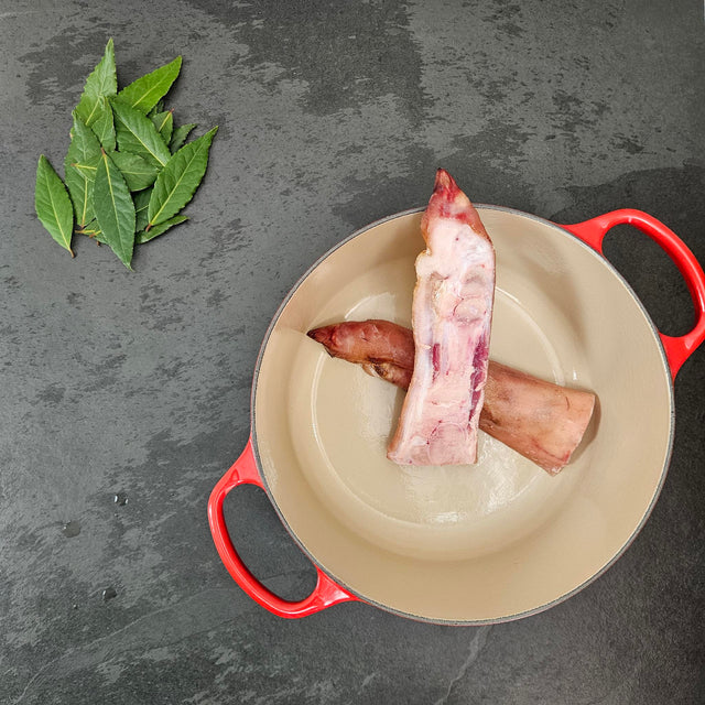 Pasture-raised split pig foot in a red Le Creuset Dutch oven with fresh bay leaves — Wishbone Heritage Farms, Saint George, SC