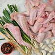 Raw pasture-raised whole chicken wings on marble with fresh scallions, garlic cloves, skewers, and chili dipping sauce — Wishbone Heritage Farms, South Carolina